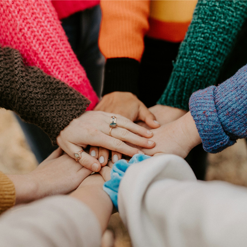 A circle of hands in an outdoor setting.